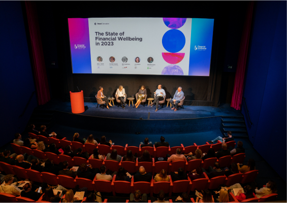 Panel discussion on the state of financial wellbeing in 2023, featuring speakers on stage in front of a large audience.
