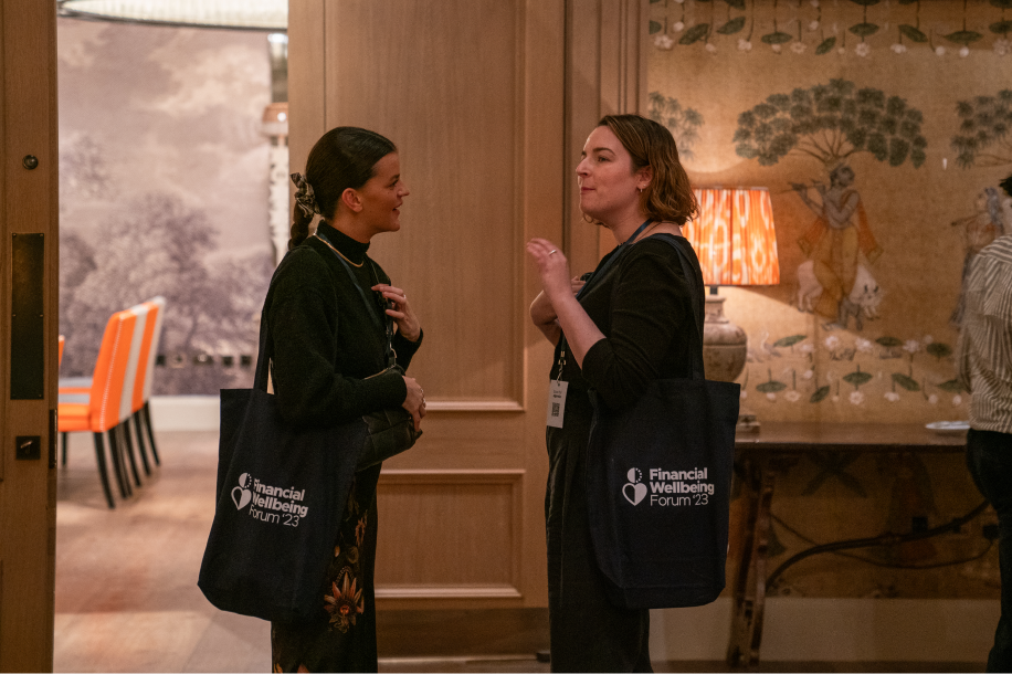 Two women at the Financial Wellbeing Forum 23, networking and holding event tote bags.
