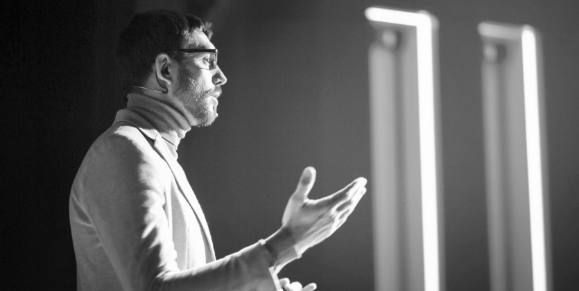 Black and white photo of a man in a suit giving a presentation.
