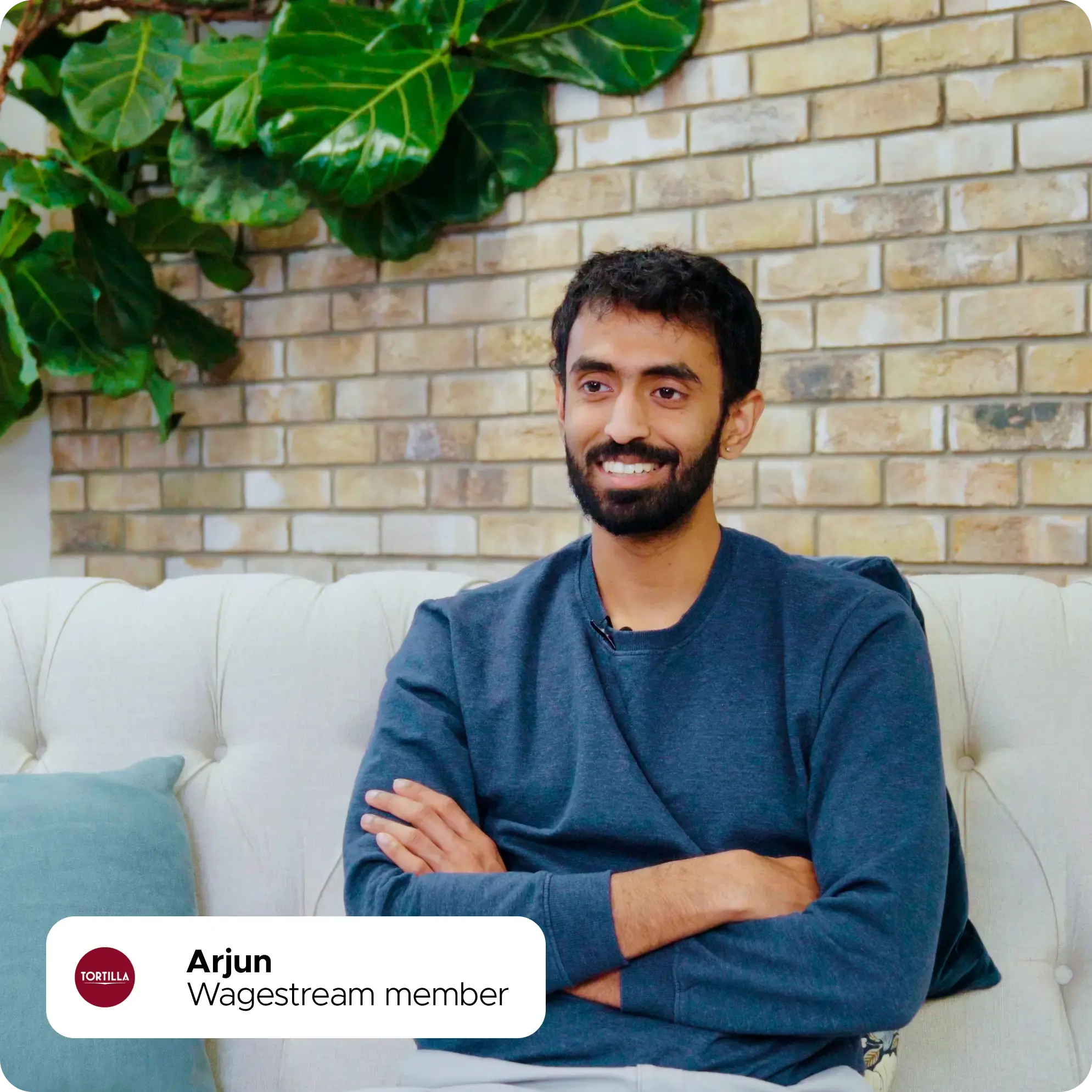 Arjun, Wagestream member, smiling and sitting on a couch with his arms crossed.
