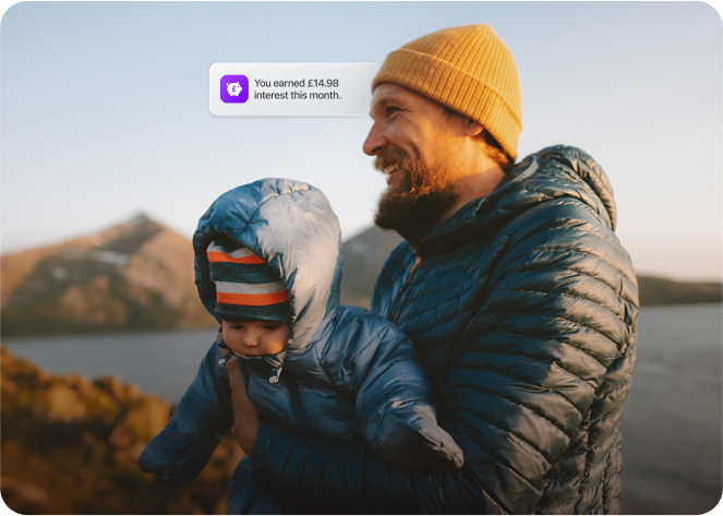 Happy father holding his baby while receiving a notification that he earned £14.98 interest this month using the Wagestream app.
