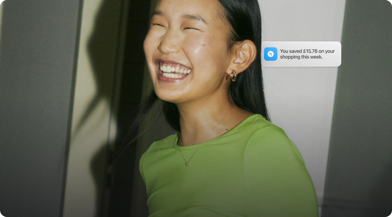 Happy woman in green shirt receiving notification that she saved £15.78 on her shopping this week using Wagestream.
