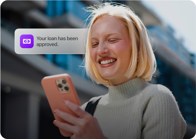 Happy woman smiling while reading a loan approval notification on her phone.
