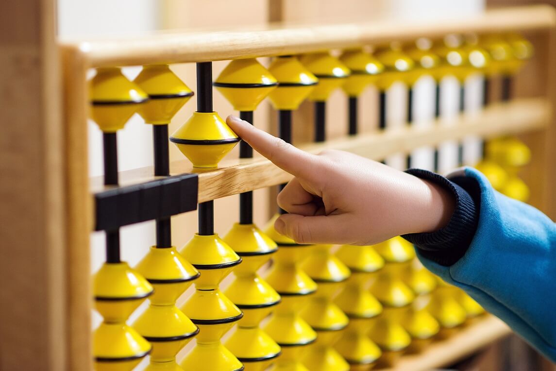 A child's hand using an abacus, demonstrating the use of a calculation tool.
