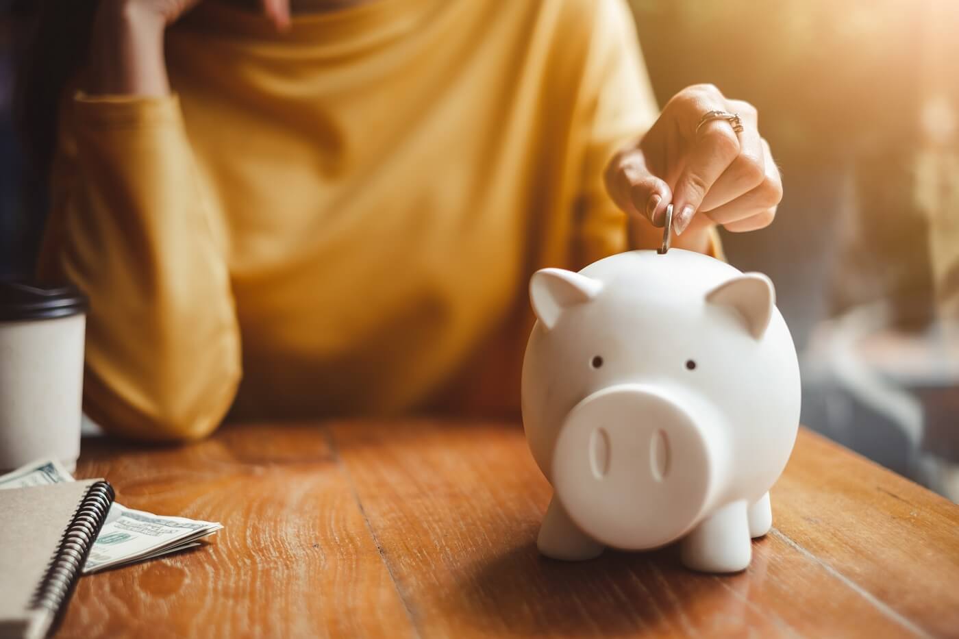 Woman putting coin in piggy bank, saving money for financial wellness.
