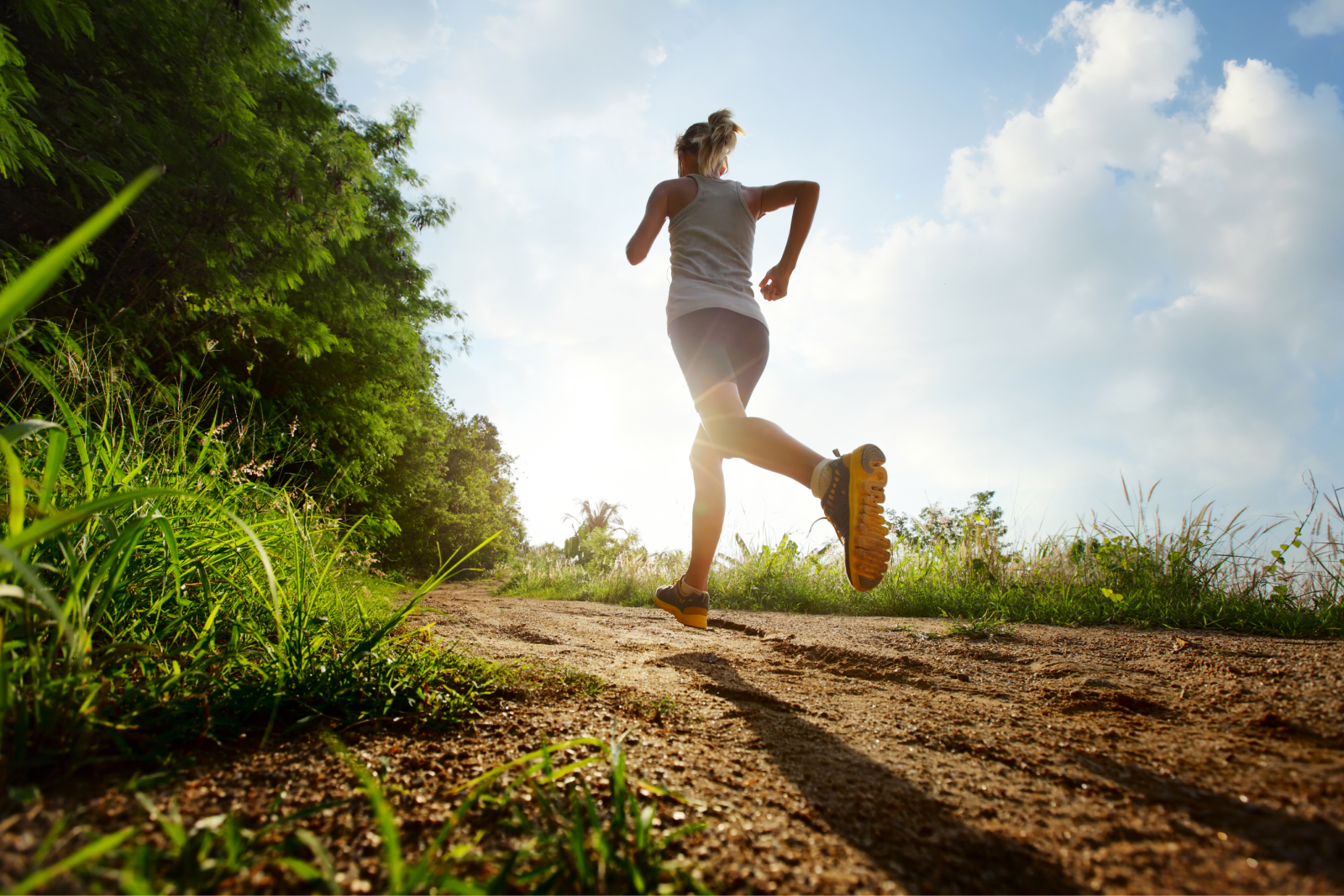 Woman jogging on a trail, enjoying the outdoors and sunshine.
