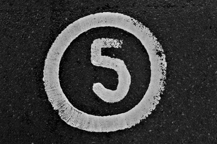 A white painted number five inside a white circle on dark asphalt.
